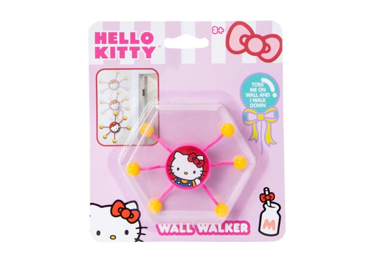 A Hello Kitty-themed wall walker toy in pink packaging. The toy has a central Hello Kitty face and six yellow suction cups. Text on the package reads "Hello Kitty Wall Walker." Illustration shows the toy sliding down a wall.