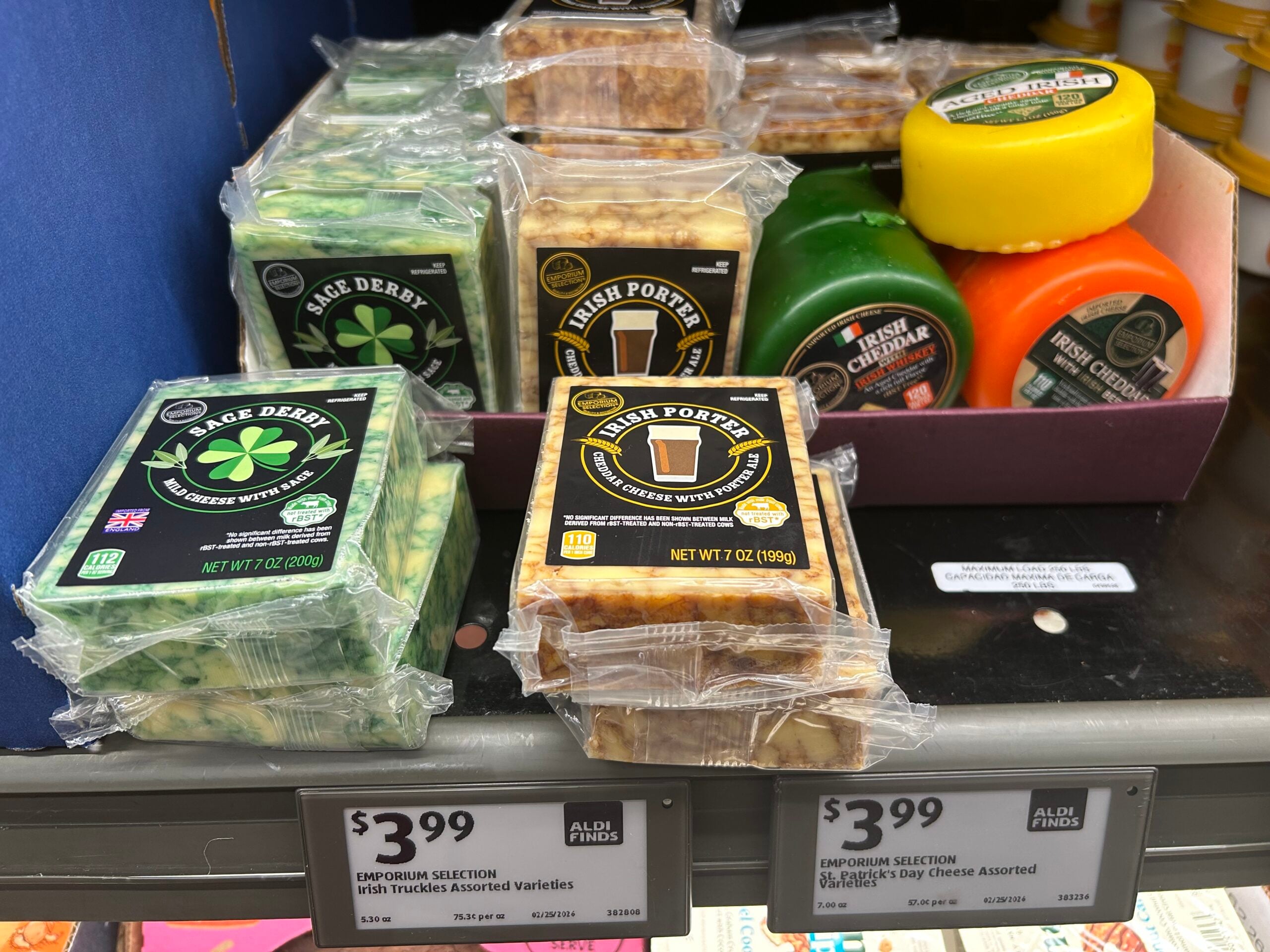 Assorted specialty cheeses, including Sage Derby, Irish Porter, and colored cheese wheels, are displayed on a store shelf with $3.99 price tags and ALDI Finds labels.