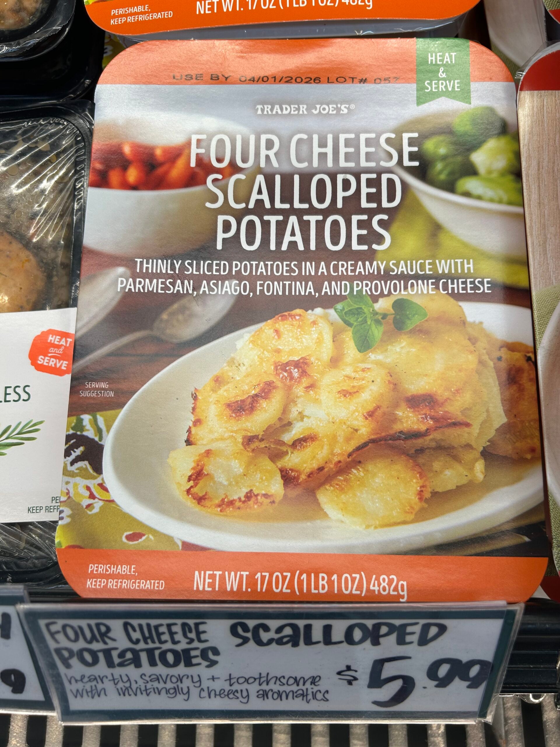 Packaging of Trader Joe’s Four Cheese Scalloped Potatoes, featuring an image of creamy, baked scalloped potatoes on a plate, garnished with herbs. The package describes the dish and lists the price as $5.99.