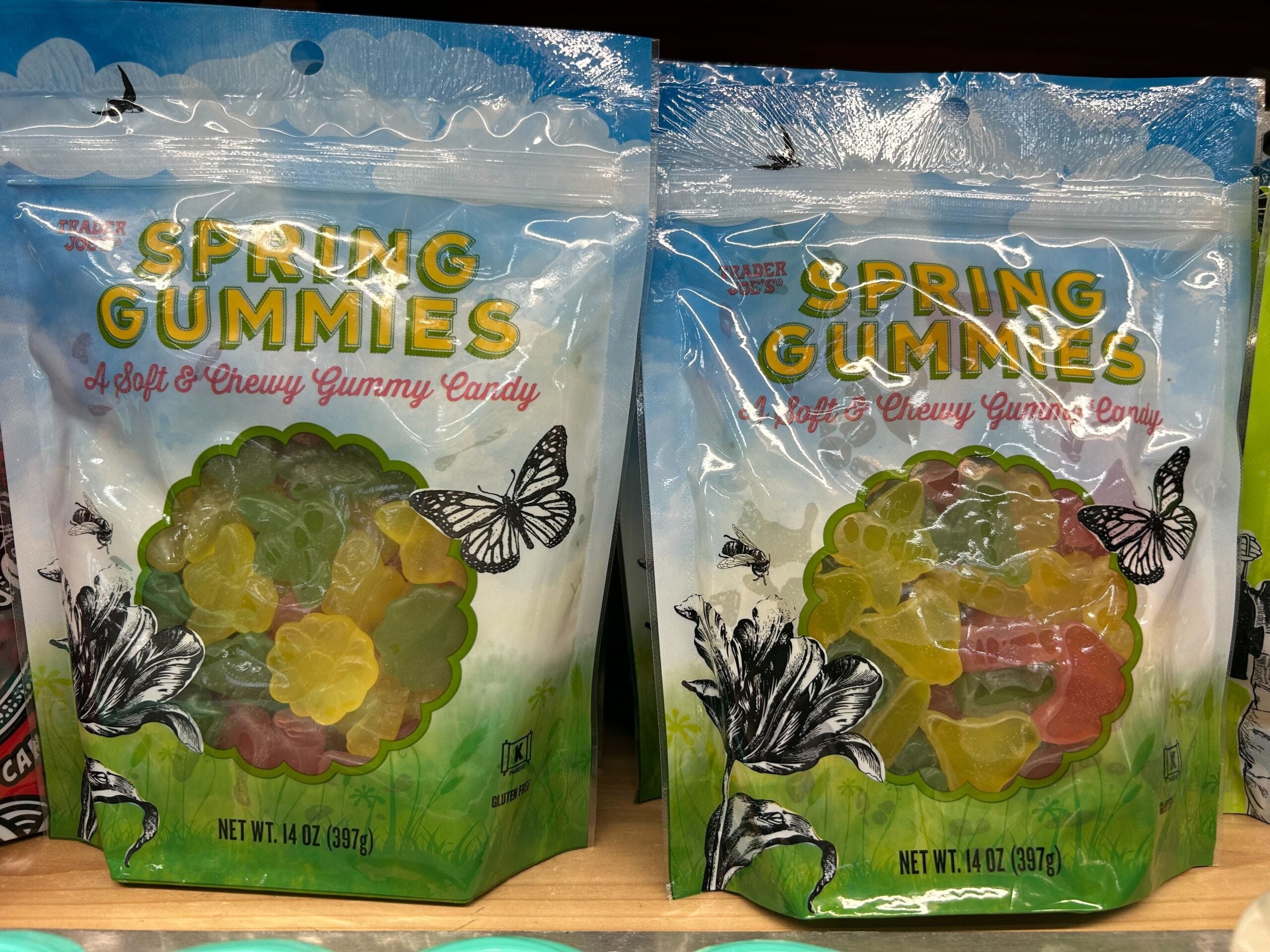 Two bags of "Spring Gummies" soft and chewy gummy candy are displayed. The packaging features colorful gummy shapes, green grass, and black-and-white butterflies on a blue sky background. Each bag is 4.4 oz (397 g).