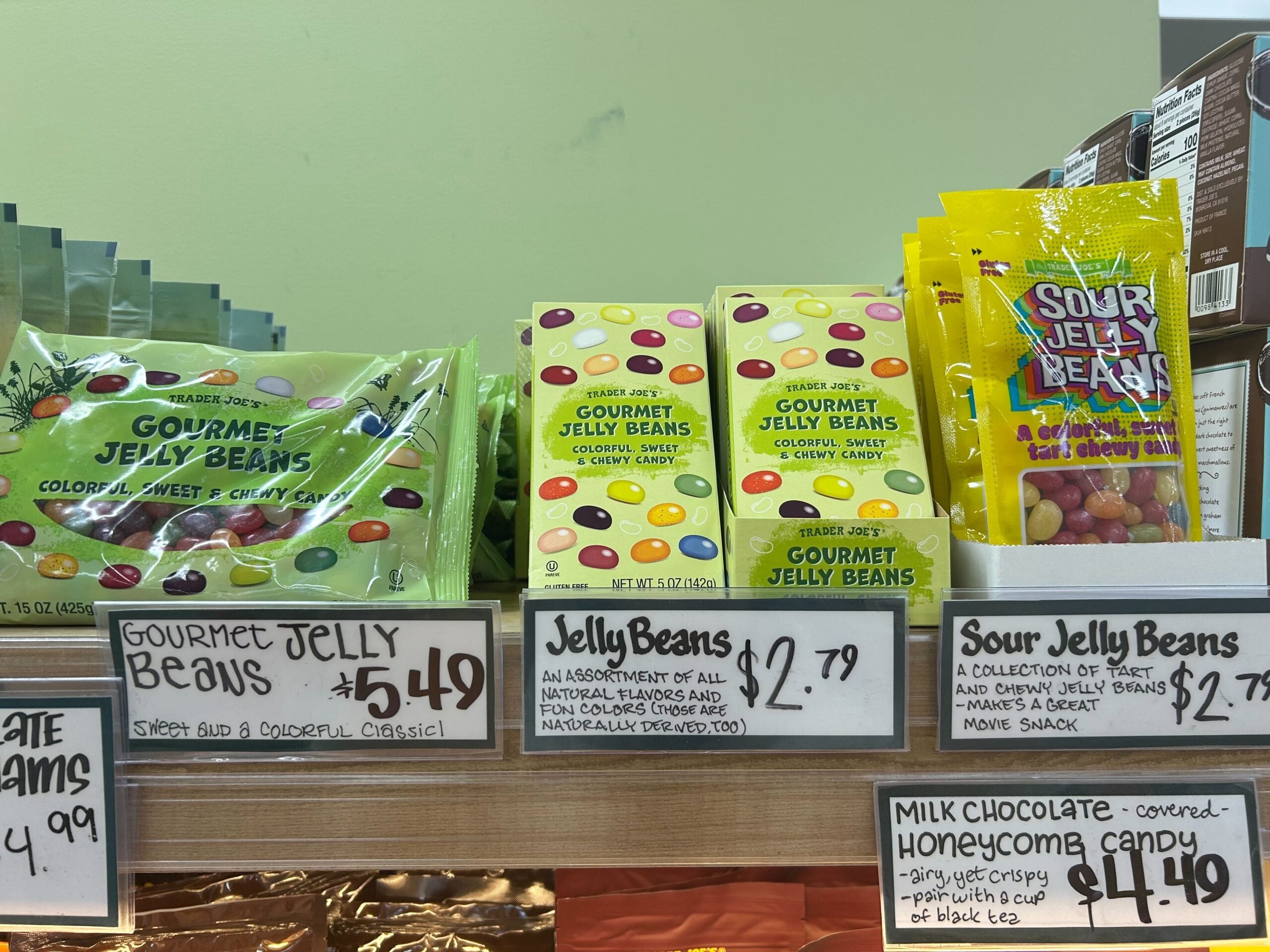 A display of colorful jelly bean packages with handwritten price tags, including "Gourmet Jelly Beans" for $5.49, "Jelly Beans" for $2.79, and "Sour Jelly Beans" for $4.49 on a store shelf.