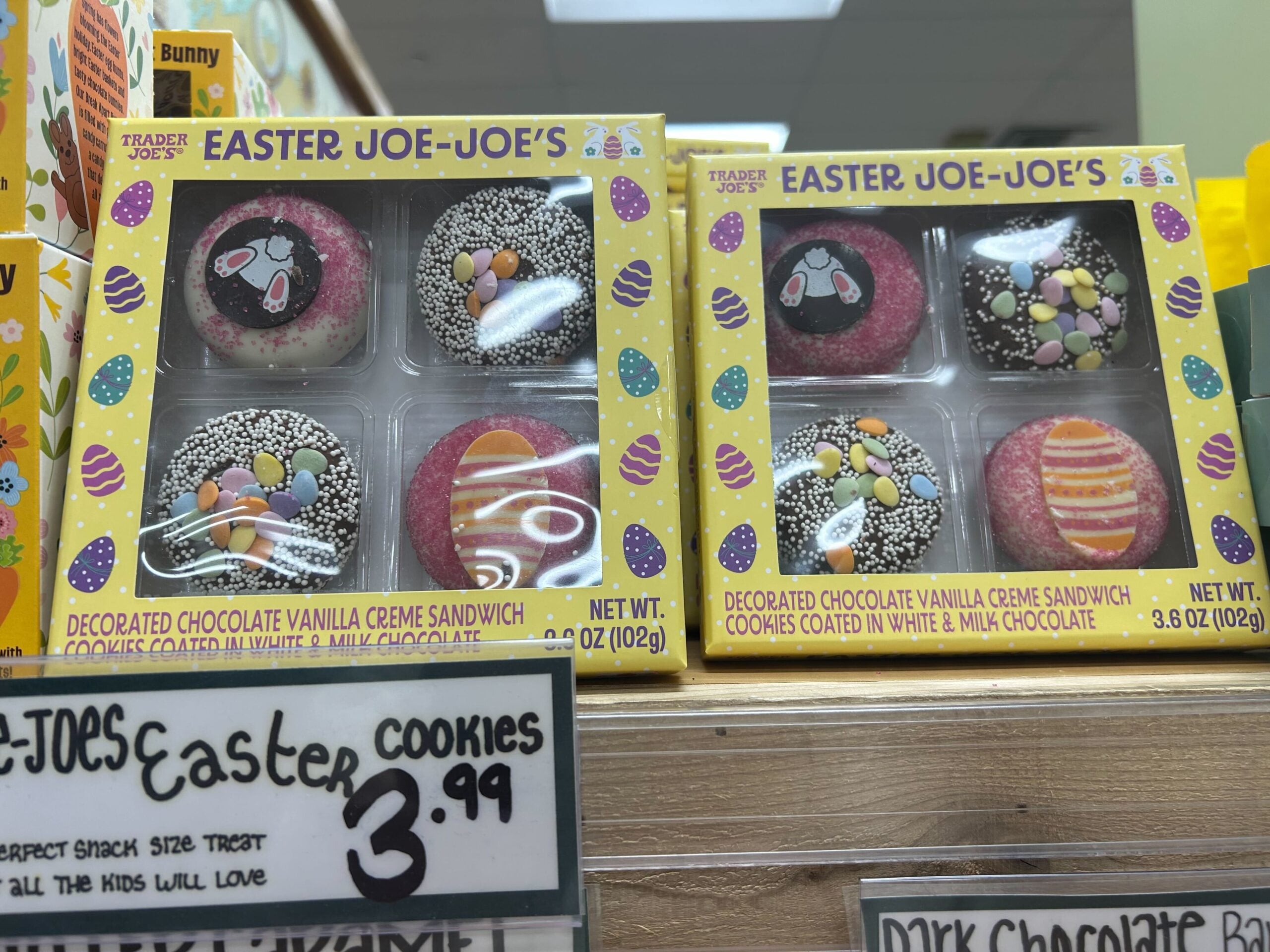 Two boxes of Trader Joe's Easter Joe-Joe's decorated chocolate vanilla creme sandwich cookies, each featuring festive designs like eggs and bunnies. A price sign below reads "Easter cookies $3.99".