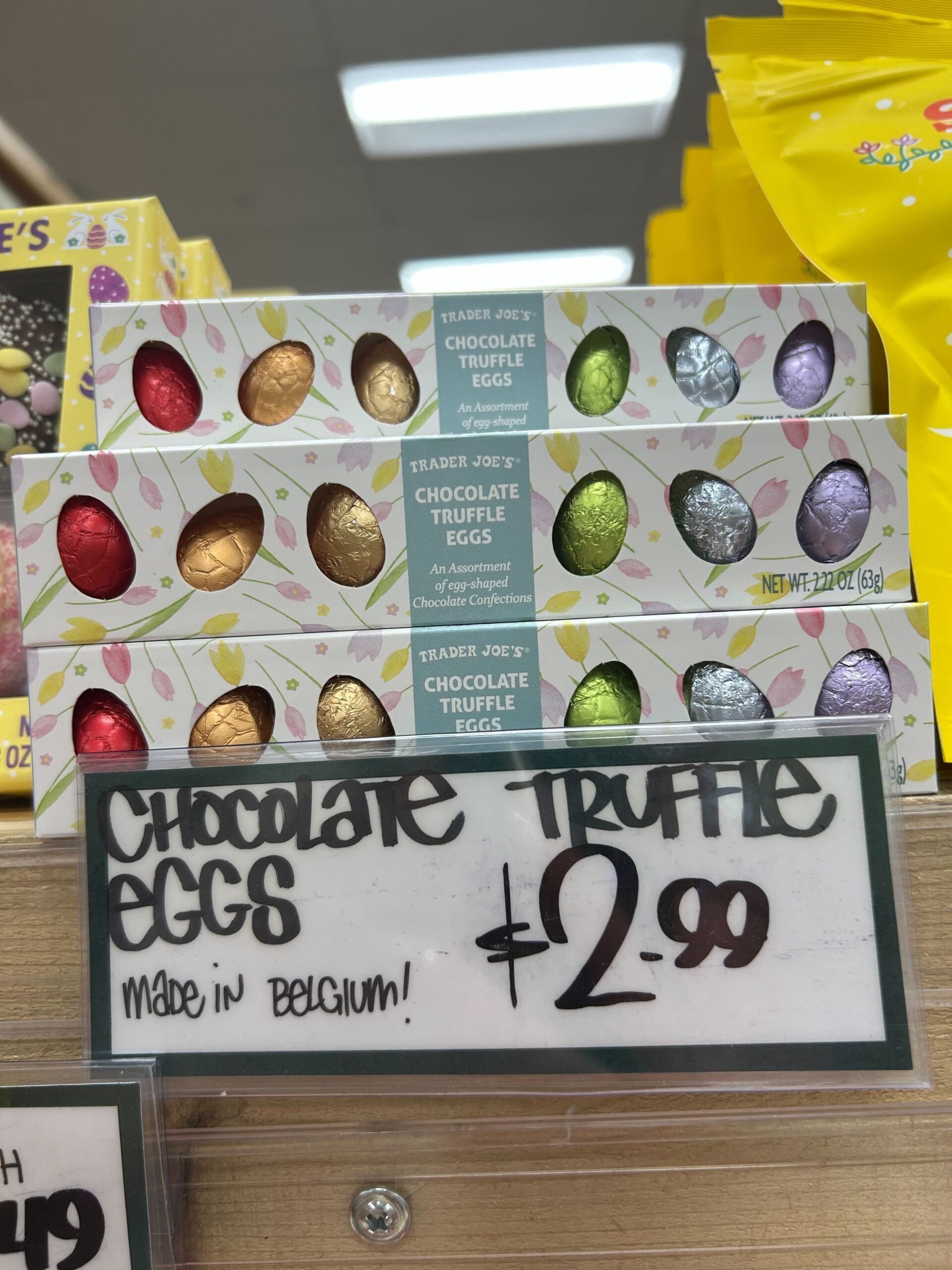 Boxes of Trader Joe's Chocolate Truffle Eggs, each containing six foil-wrapped eggs, are displayed on a shelf with a sign below reading "Chocolate Truffle Eggs $2.99 Made in Belgium!