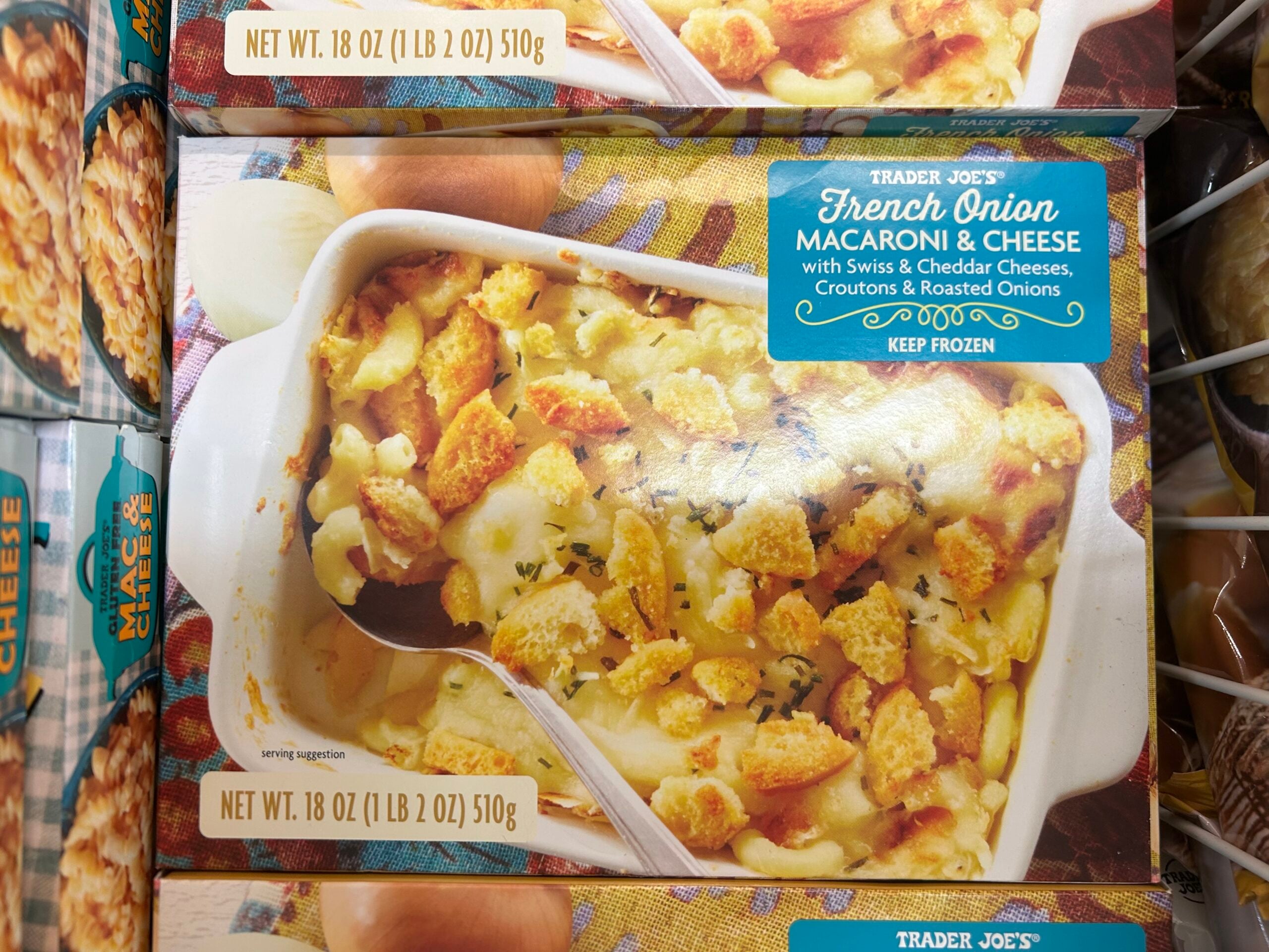 A box of Trader Joe’s French Onion Macaroni & Cheese, featuring an image of the dish in a white baking dish, topped with melted cheese, croutons, and herbs. The package highlights its Swiss and Cheddar cheeses.