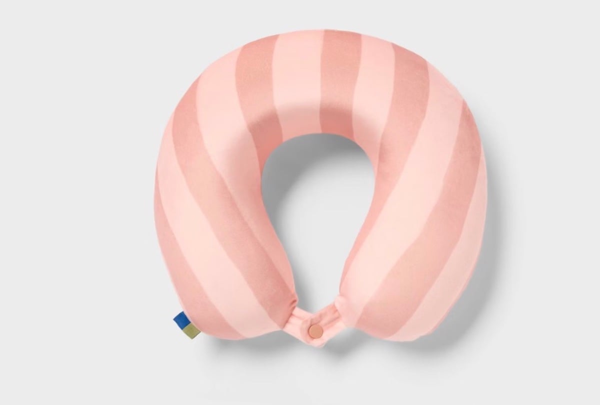 A pink and light pink striped U-shaped travel neck pillow with a button closure at the front, perfect for spring break getaways, displayed on a light gray background.