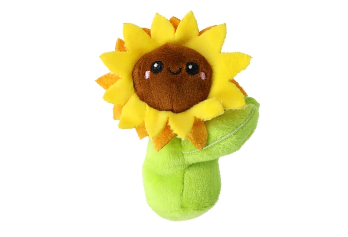 A plush toy shaped like a sunflower with a smiling face, brown center, bright yellow petals, and a soft green stem and leaves, set against a plain white background.