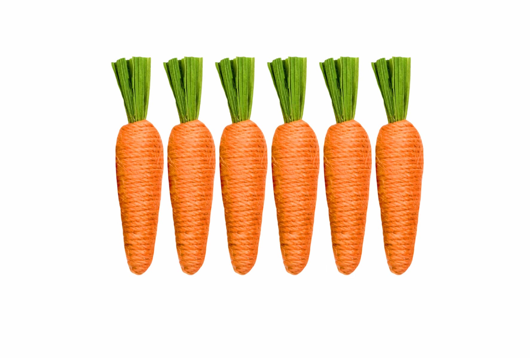 Six artificial carrots made of orange and green textured materials are arranged in a row on a white background. The carrots are evenly spaced and identical in shape and size.