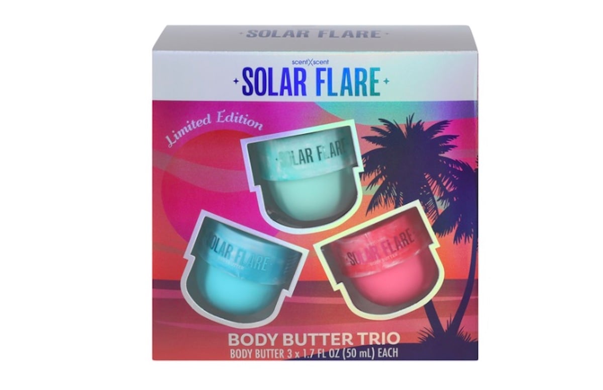 A box of SOLAR FLARE Limited Edition Body Butter Trio beauty products featuring three jars in teal, blue, and pink, set against a tropical sunset with palm tree silhouettes. Includes 3 x 1.7 fl oz (50 ml) jars.