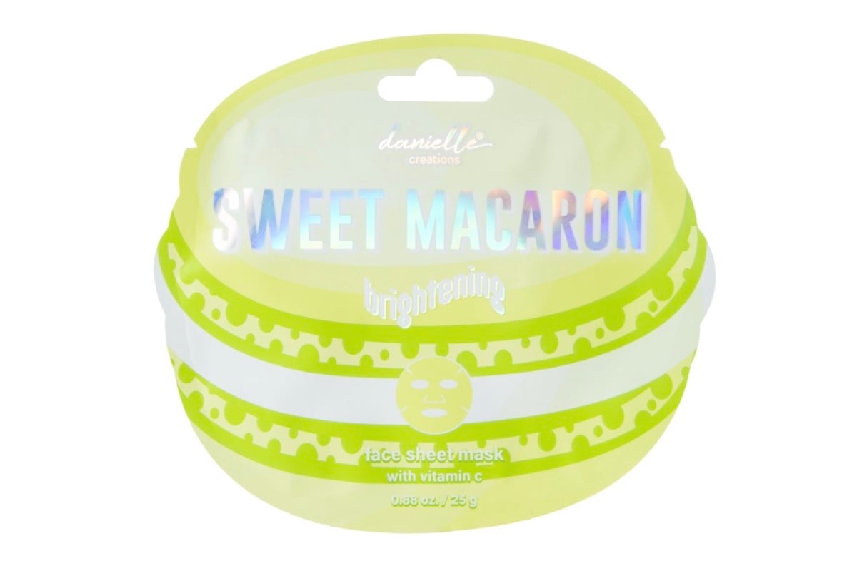 Front view of a “Sweet Macaron” brightening face sheet mask package by Danielle Creations, designed to look like a yellow-green macaron, with holographic text and vitamin C mentioned on the label.
