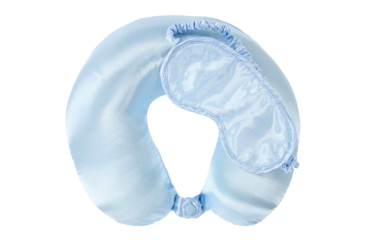 A light blue satin travel neck pillow with a matching satin sleep mask resting on top, both designed for comfort during travel—one of those five below finds perfect for your next trip.