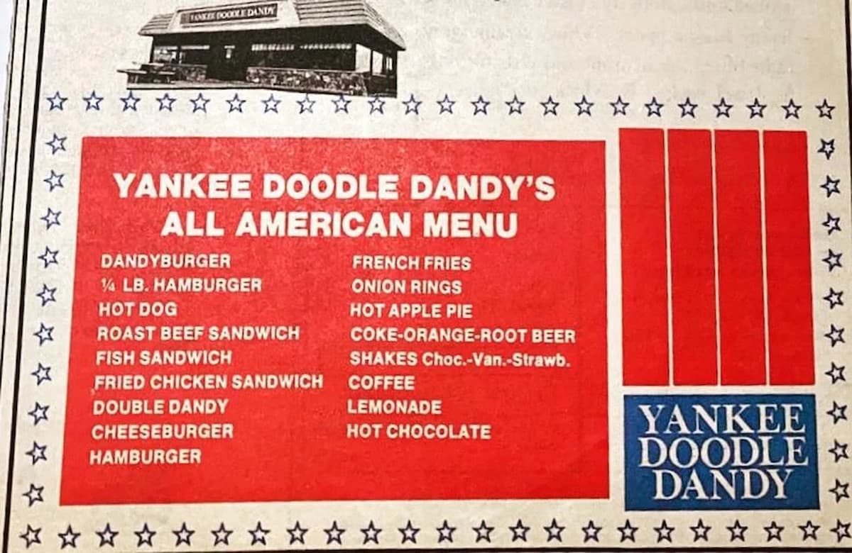 A vintage Yankee Doodle Dandy’s All American Menu lists items like burgers, hot dogs, sandwiches, fries, shakes, apple pie, and drinks, with a red, white, and blue patriotic design and a restaurant image at the top.