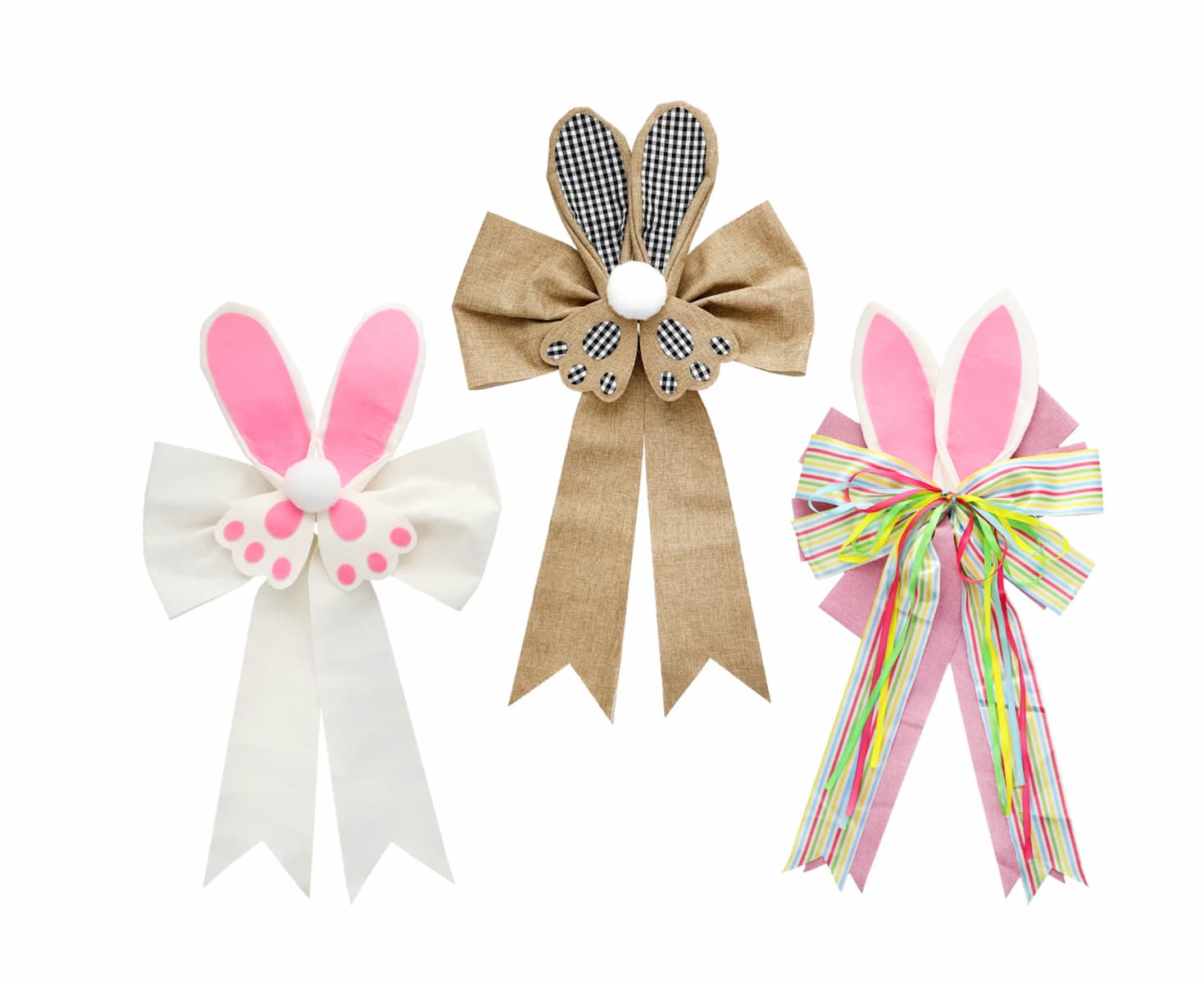 Three decorative bows with bunny ears: one white with pink ears and paw prints, one brown with checkered ears and white pom-pom, and one pink with striped ribbon and white-pink ears, all on a white background.