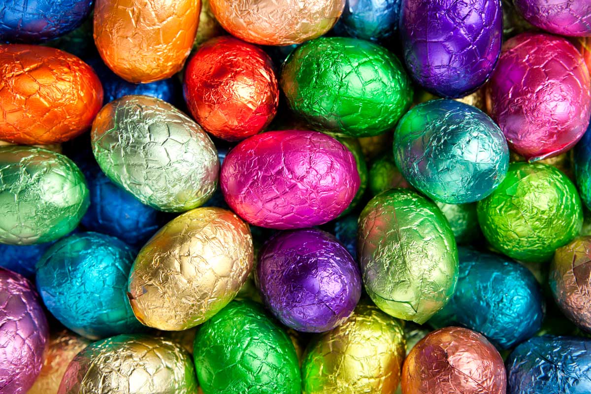 Colorful foil-wrapped chocolate eggs, like those found in Dollar Tree Easter candy aisles, are closely packed together, creating a vibrant and festive arrangement with shiny wrappers in green, gold, purple, pink, blue, orange, and red.