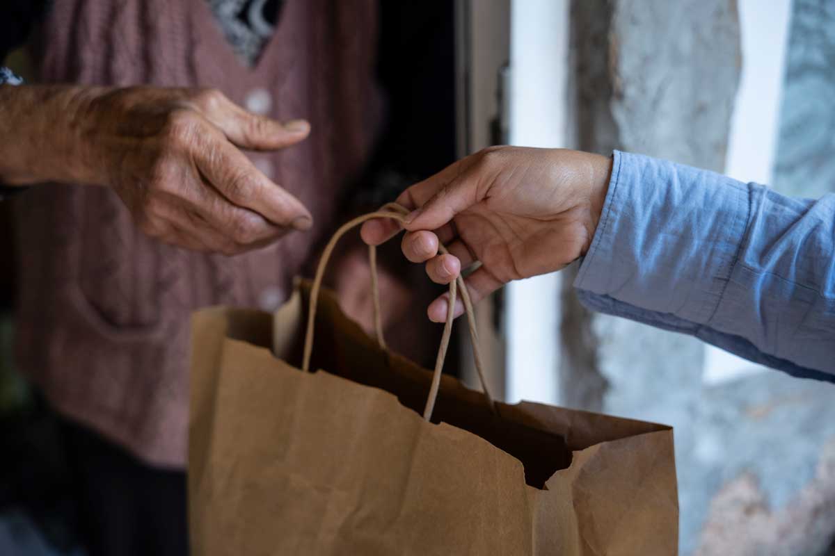 A close-up of two people’s hands exchanging a brown paper bag at a doorway, suggesting an Uber Eats delivery or gift being handed over from one person to another.