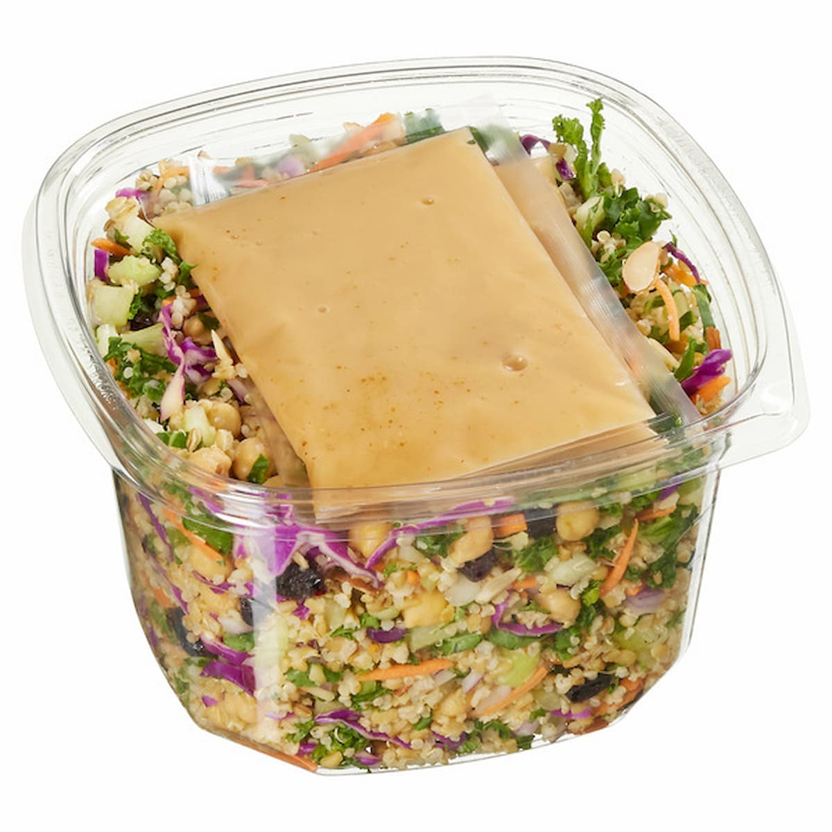 A clear plastic container filled with a colorful salad, including greens, cabbage, nuts, and grains, topped with a rectangular packet of dressing. The container has a hinged lid.
