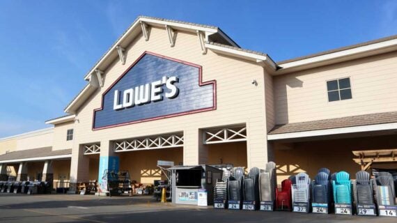 The exterior of a Lowe&rsquo;s store on a sunny day, with the large Lowe&rsquo;s sign above the entrance and stacks of colorful patio chairs and outdoor items&mdash;perfect for customers exploring their maintenance subscription service.