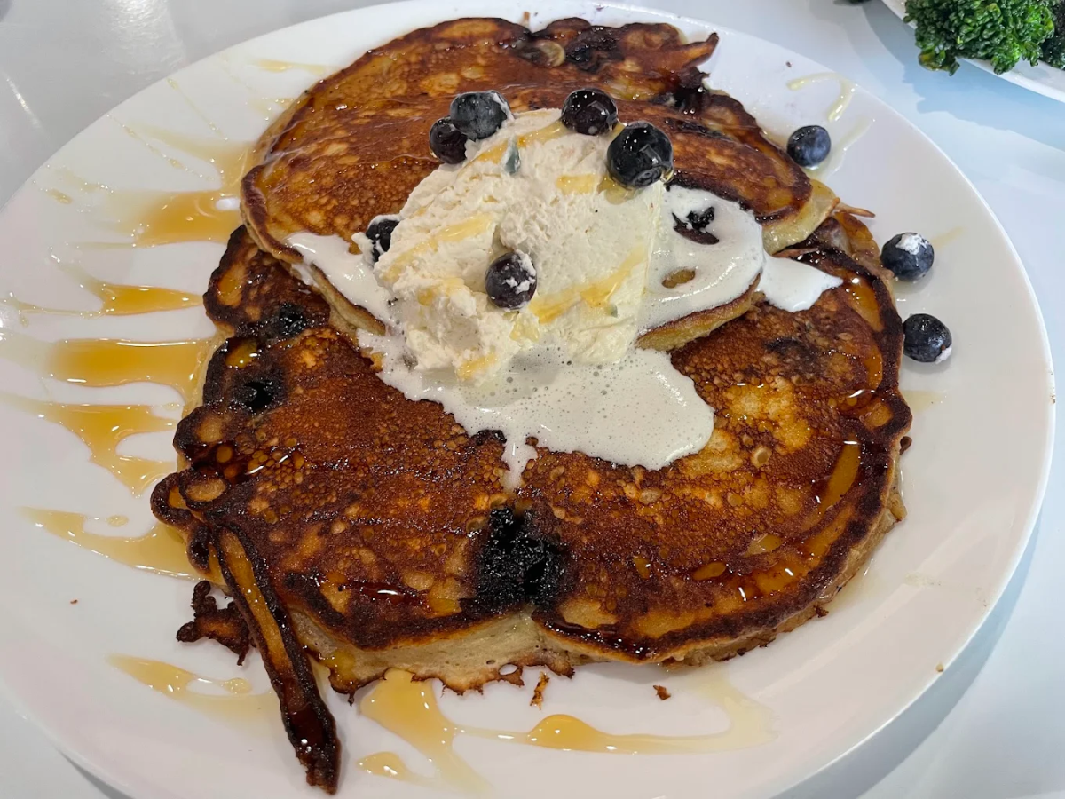 A plate of golden-brown pancakes topped with a scoop of vanilla ice cream, fresh blueberries, and drizzled with syrup.