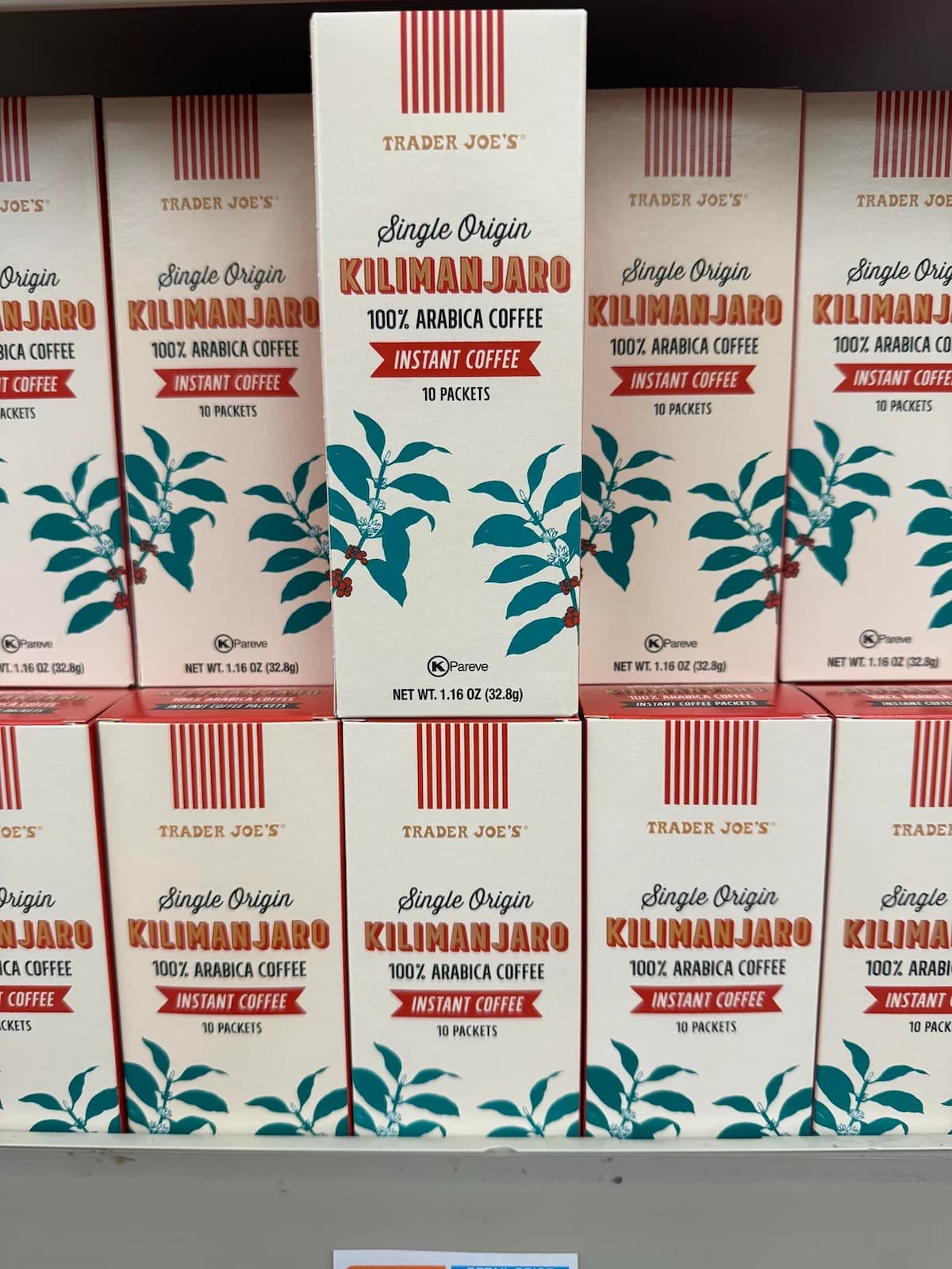 Boxes of Trader Joe’s Single Origin Kilimanjaro 100% Arabica Instant Coffee are stacked on a shelf; the packaging is cream-colored with red text and teal coffee plant illustrations.
