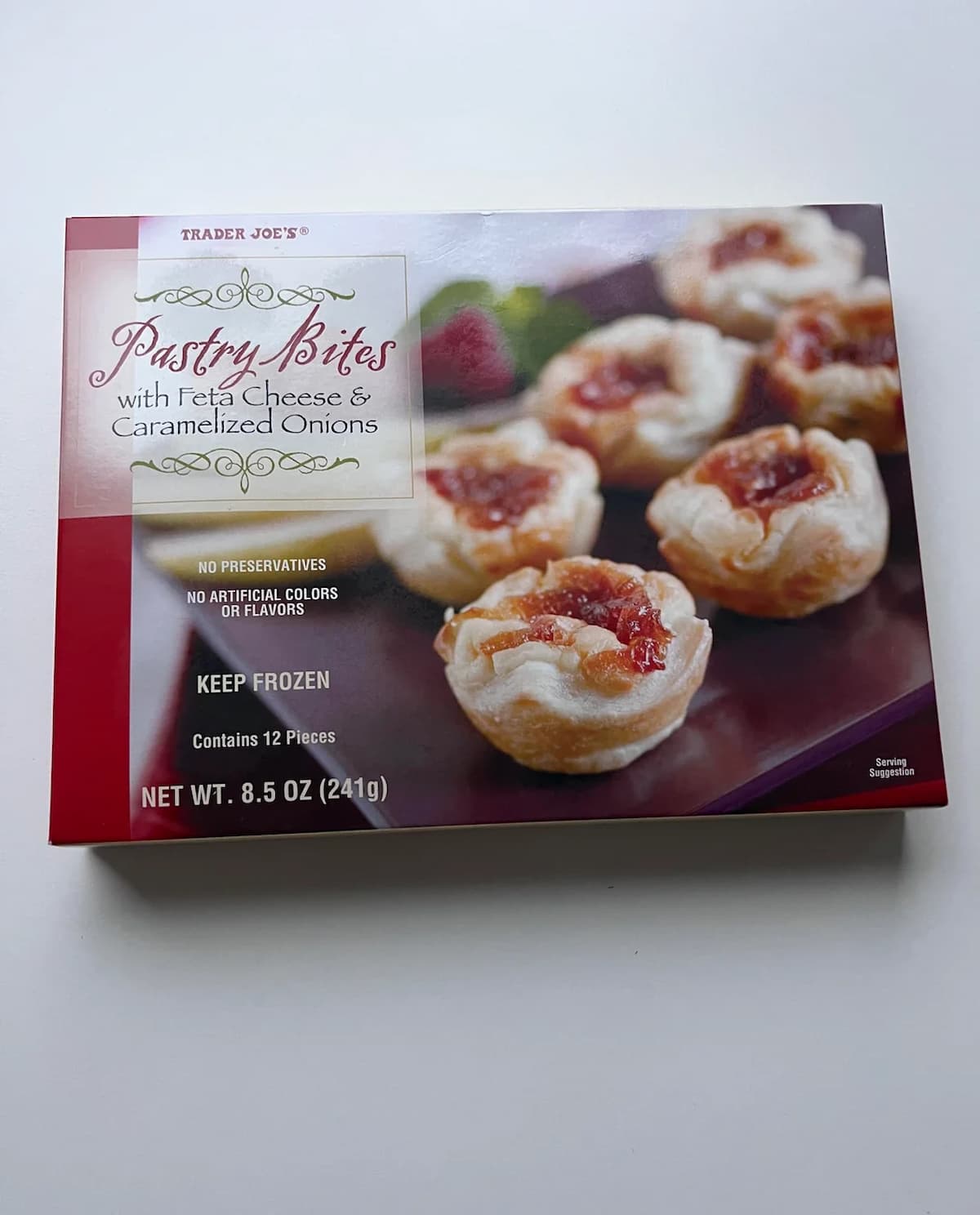 A box of Trader Joe’s Pastry Bites with Feta Cheese & Caramelized Onions, showing an image of the pastry bites on the front. The box notes no preservatives and contains 12 frozen pieces, net weight 8.5 oz (241g).