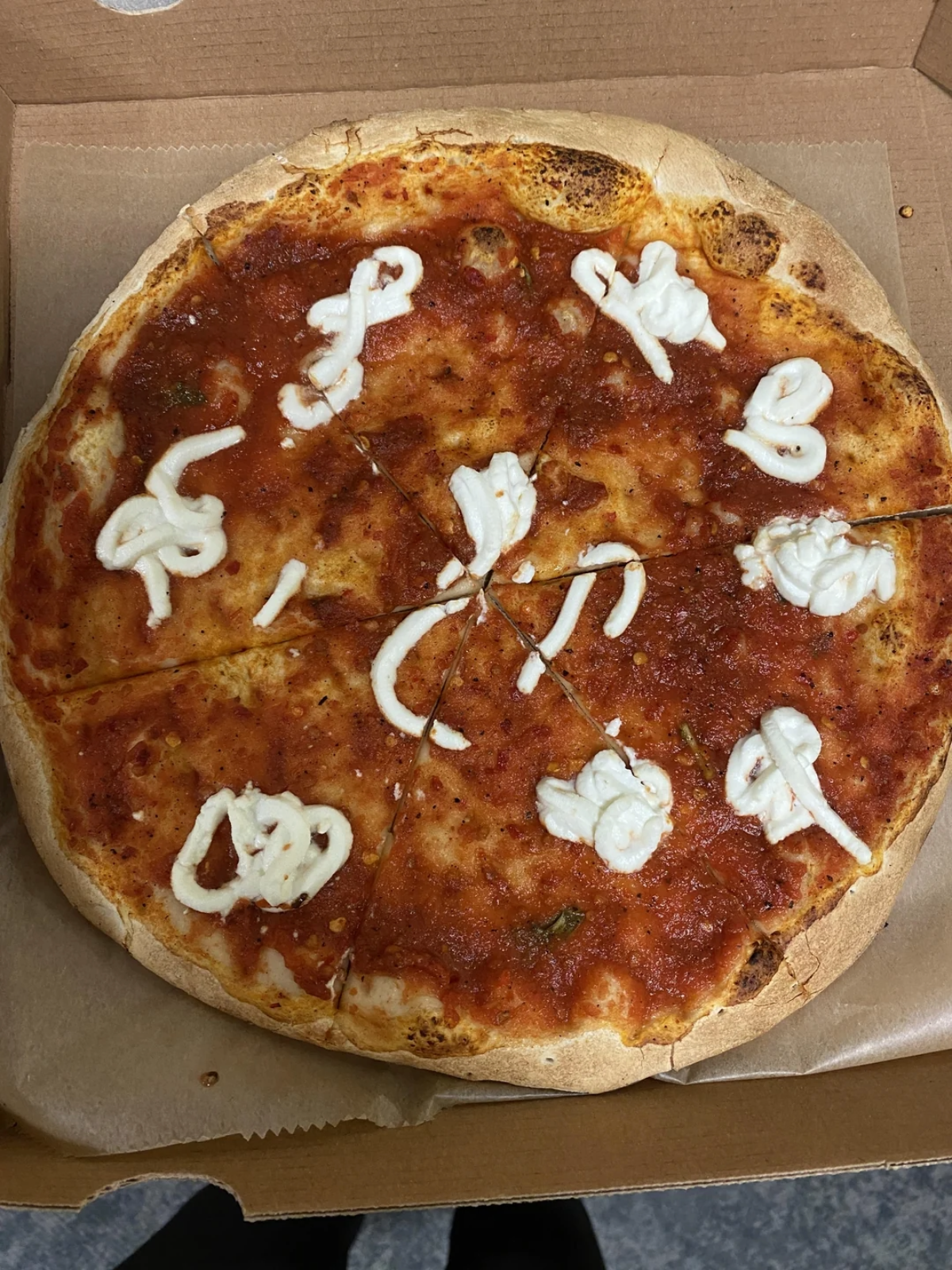 A pizza in a cardboard box with tomato sauce and small, uneven blobs of white cheese spread across the slices, but with most of the pizza surface bare, showing minimal toppings.