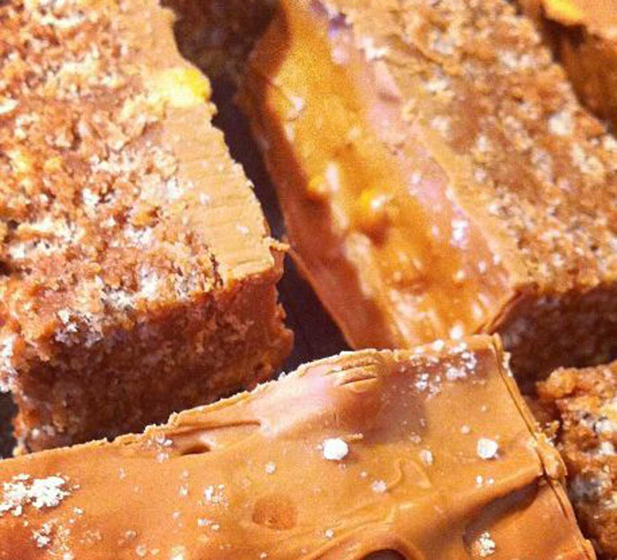 Close-up of chocolate bars with a caramel and nougat filling, showing a cross-section of the layered interior and a dusting of sugar on top.