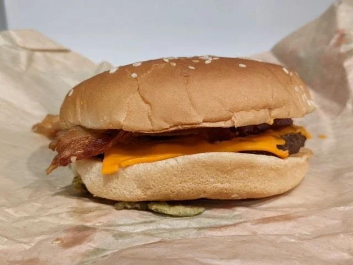 A cheeseburger with a sesame seed bun, crispy bacon, a slice of cheddar cheese, and a beef patty sits on a crumpled sheet of brown sandwich paper.