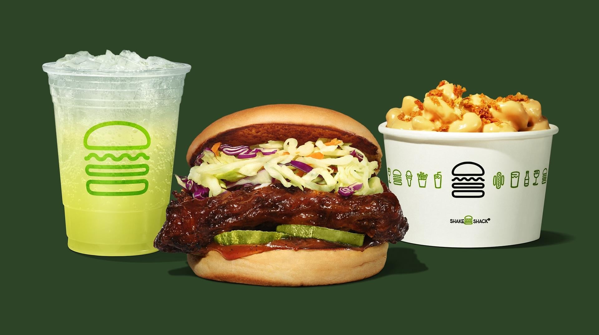 A cold green drink, a barbecue chicken sandwich with pickles and slaw, and a cup of macaroni and cheese with crispy topping, all featured on a vibrant green background—perfect picks from the new fast-food menu.