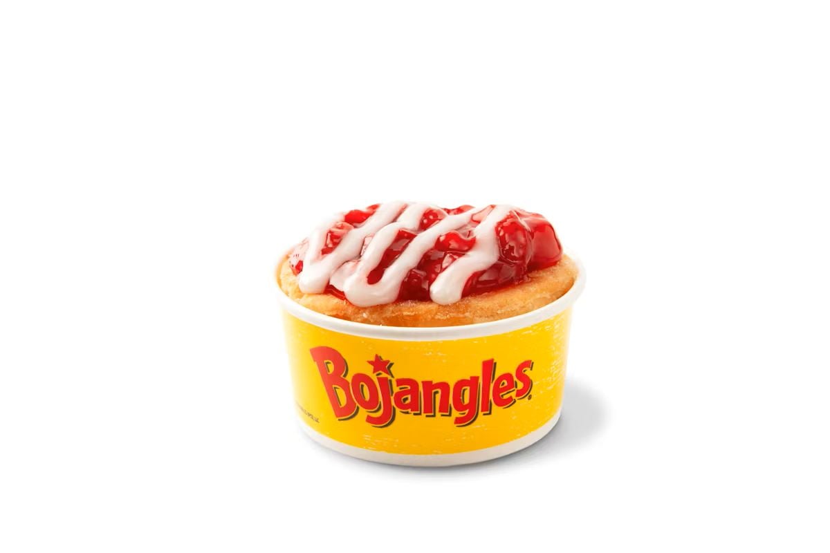 A new fast-food menu treat: a Bojangles dessert in a yellow cup, topped with red fruit filling and white icing drizzle, placed against a white background.