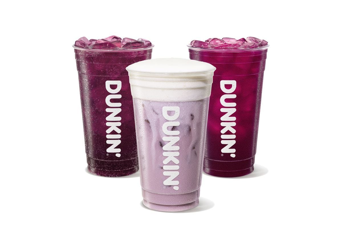 Three tall Dunkin' drinks from the new fast-food menu are shown: two purple iced beverages with ice and one light purple iced drink topped with a layer of white foam. All cups display the Dunkin' logo vertically.