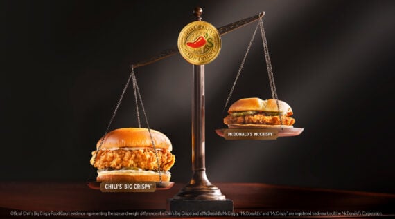 A balance scale comparing two chicken sandwiches: Chili&rsquo;s Big Crispy on the left side, which is heavier and lower, and McDonald&rsquo;s McCrispy on the right, which is lighter and higher. The background is dark.