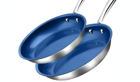 Two stainless steel frying pans with shiny blue nonstick interiors are stacked together, each with a metal handle attached with rivets. The pans are clean and reflect light.