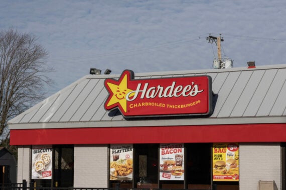 A Hardee&rsquo;s fast food restaurant with a red and yellow sign reading &ldquo;Hardee&rsquo;s Charbroiled Thickburgers&rdquo; sits under a gray roof. Despite rumors of bankruptcy, menu posters remain visible in the windows below the sign.
