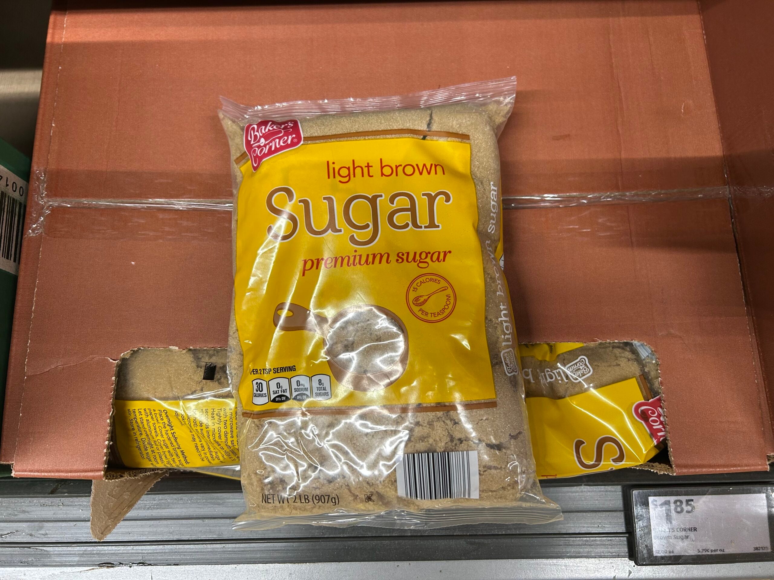 A bag of Baker's Pantry light brown premium sugar is on a store shelf, with some of the packaging torn and sugar spilling out. The price label is visible in the bottom right corner.