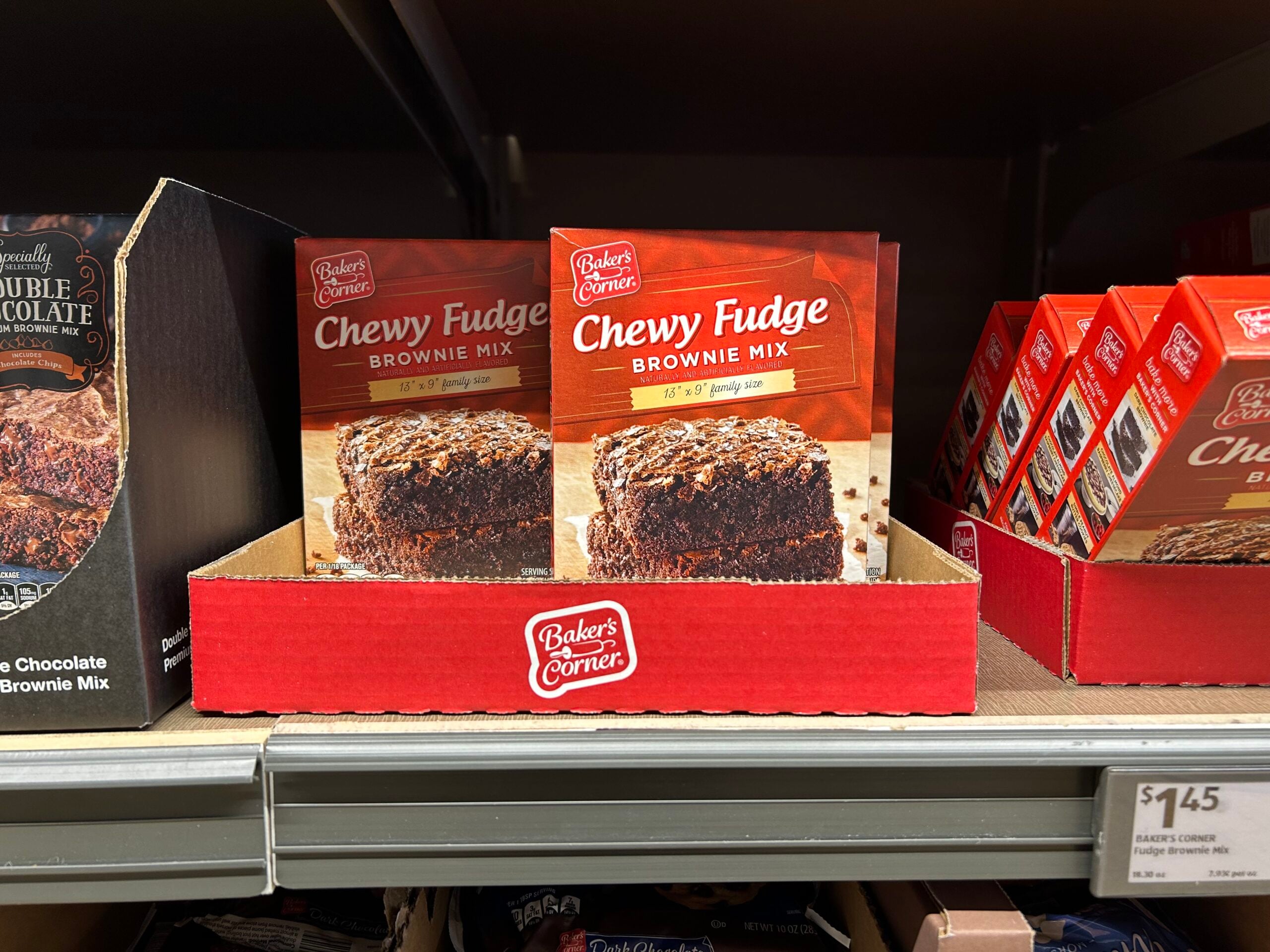 A box of Baker’s Corner Chewy Fudge Brownie Mix displayed on a store shelf with other baking mixes nearby. The price tag below reads $1.45.