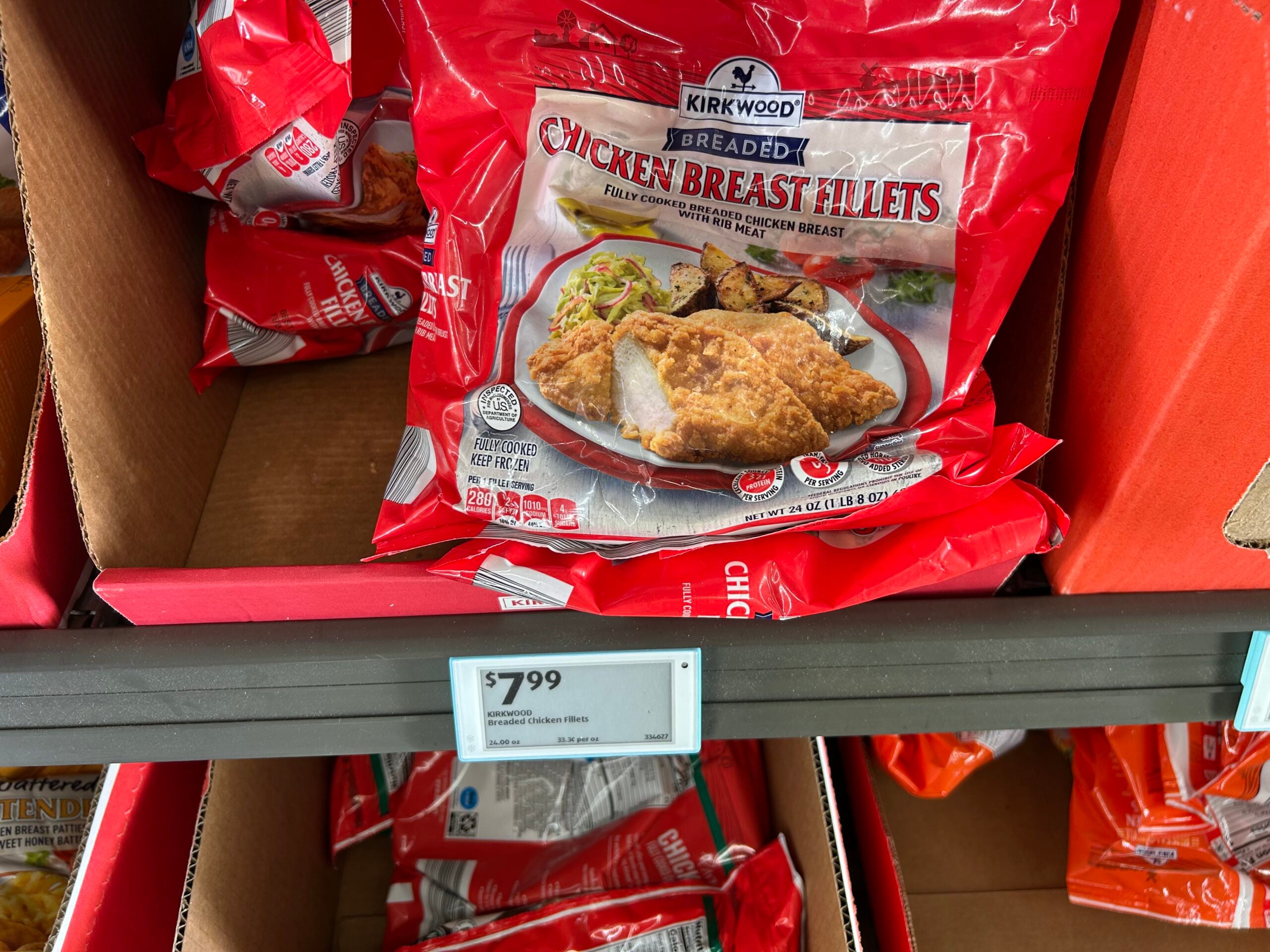 A red bag of Kirkwood Breaded Chicken Breast Fillets sits on a store shelf, priced at $7.99. The bag shows an image of breaded chicken fillets with mashed potatoes and green beans.