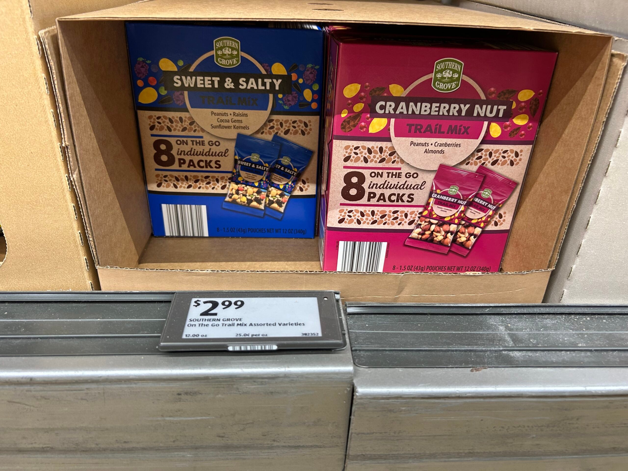 Two boxes of Southern Grove trail mix—Sweet & Salty and Cranberry Nut—are on a store shelf. Each box contains 8 individual packs. A price tag below shows $2.99.