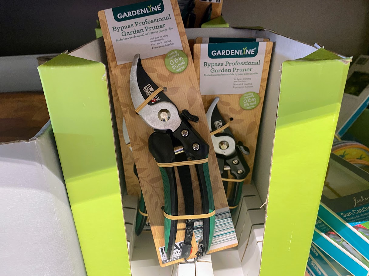 A display of Gardenline Bypass Professional Garden Pruners in green and black packaging, arranged upright in a green cardboard stand on a store shelf.