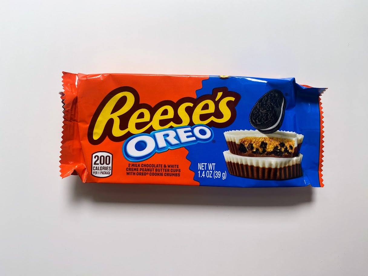 A Reese’s Oreo candy package featuring two chocolate and white creme peanut butter cups with Oreo cookie pieces, on a red and blue wrapper, labeled 200 calories per serving and weighing 1.4 oz.