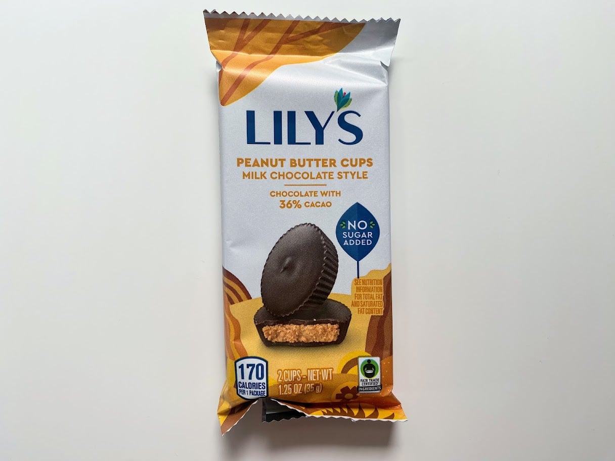 A package of Lily’s Peanut Butter Cups, Milk Chocolate Style with 36% cacao, shown on a white background. The wrapper highlights "No Sugar Added" and displays an image of the peanut butter cups.