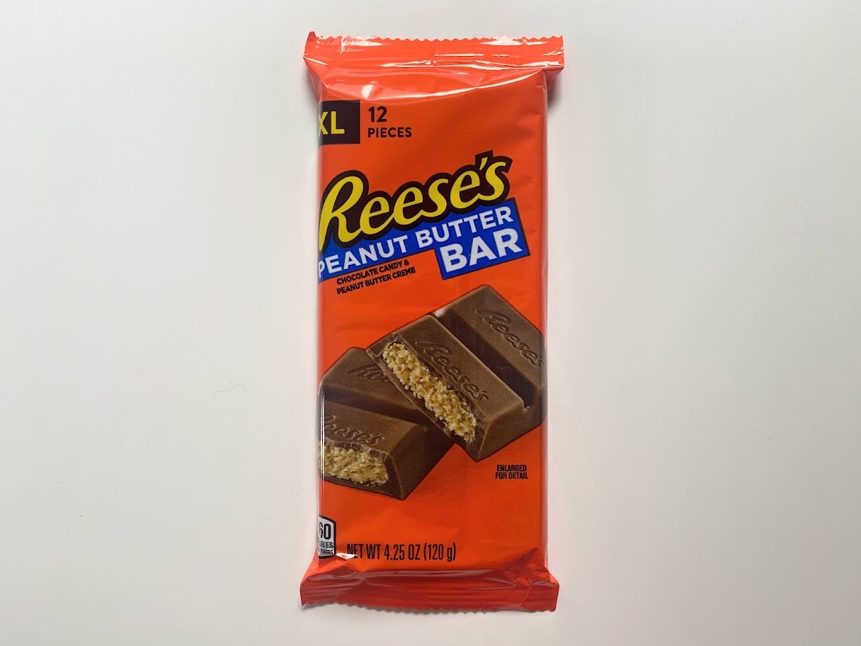 A wrapped XL Reese’s Peanut Butter Bar with 12 pieces, showing an image of the chocolate bar broken to reveal the peanut butter filling, on a bright orange package.