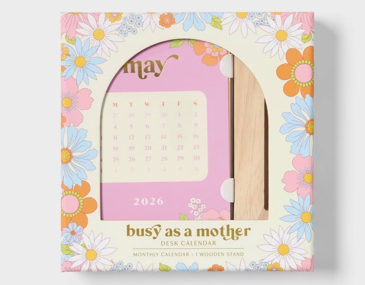 A boxed 2026 desk calendar titled "busy as a mother" with a floral border and visible May page in pink, plus a wooden stand, is displayed through a clear window—perfect for stylish organization and thoughtful Mother's Day gifts.