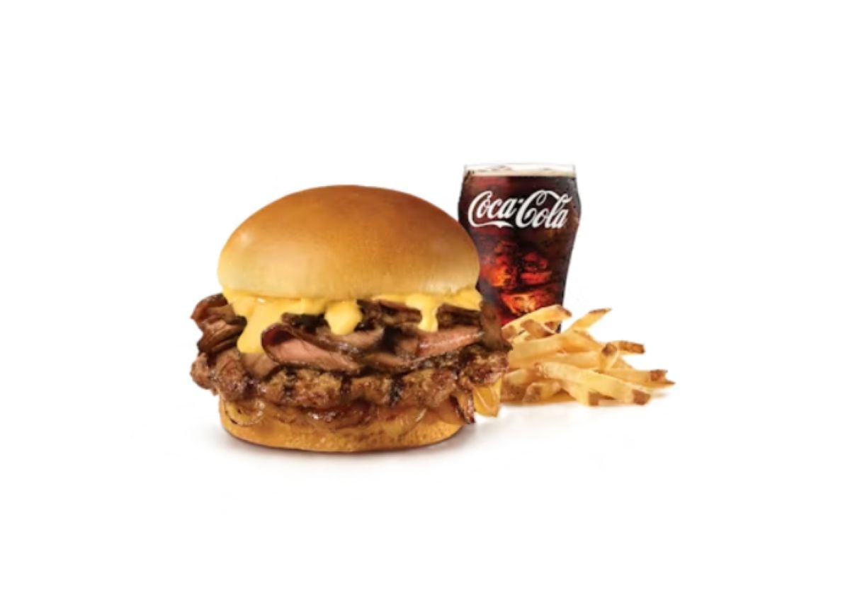 A cheeseburger with melted cheese and grilled meat from the new fast-food menu, served with a side of French fries and a glass of Coca-Cola on a white background.