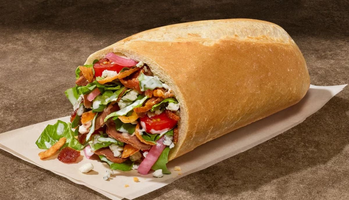 A new fast-food menu favorite: a sub sandwich filled with crispy bacon, lettuce, sliced tomatoes, red onions, and creamy dressing, all inside a thick, crusty roll and served fresh on parchment paper.