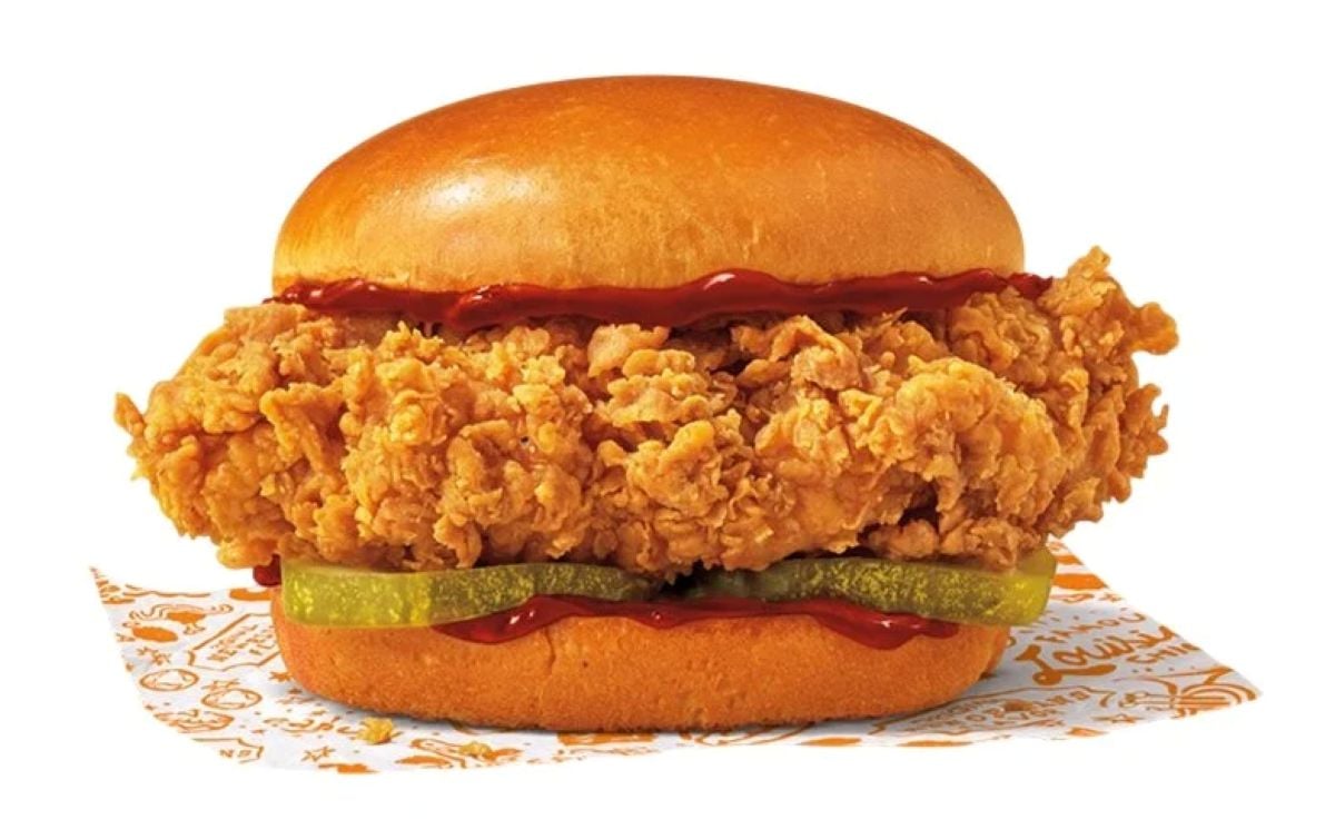 A new fast-food menu favorite: a fried chicken sandwich with a crispy chicken fillet, pickles, and ketchup on a brioche bun, served on patterned paper with an orange and white design.