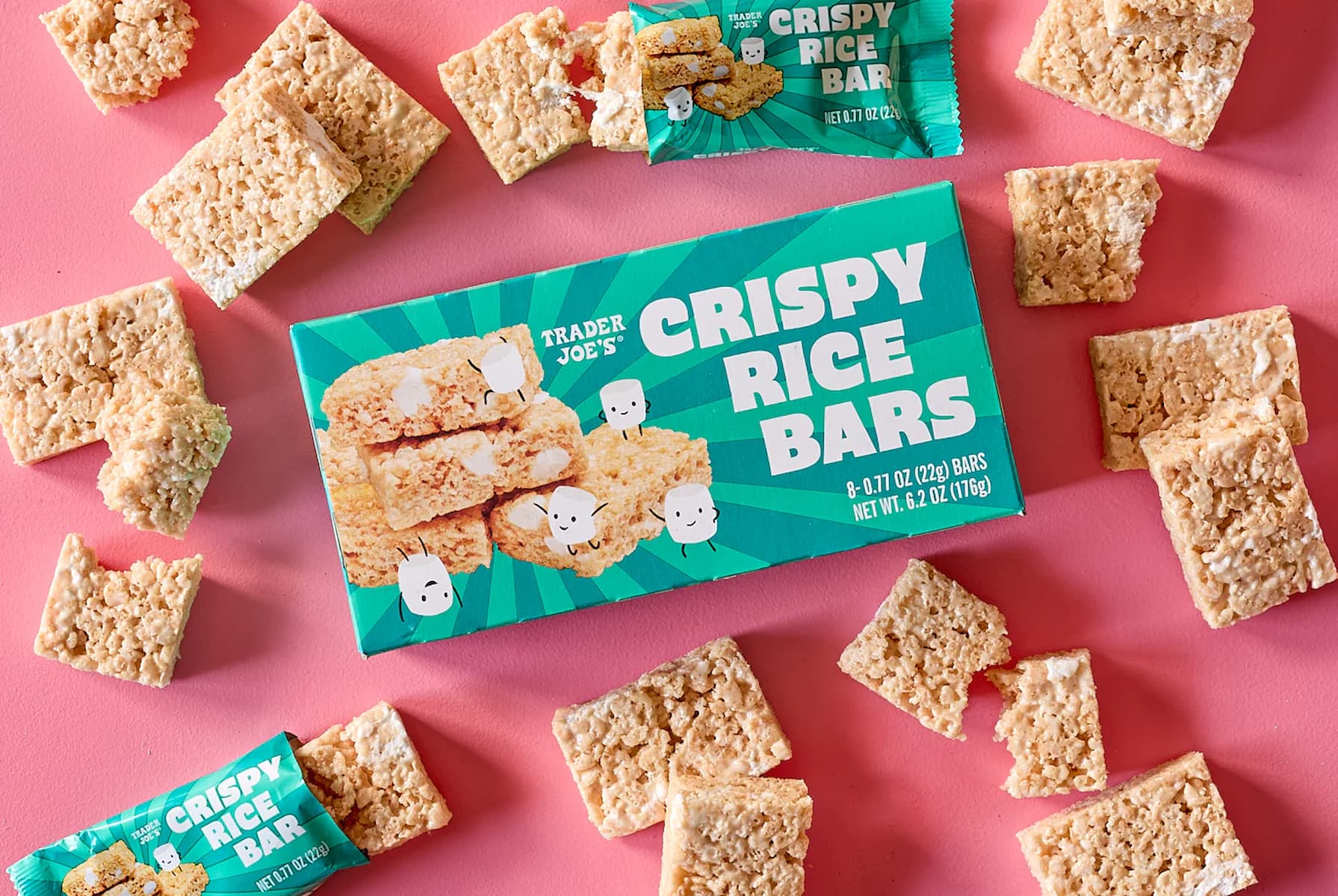 A box of Trader Joe's Crispy Rice Bars is surrounded by unwrapped bars and pieces on a pink background. Some bars are whole, others are broken or partially unwrapped.