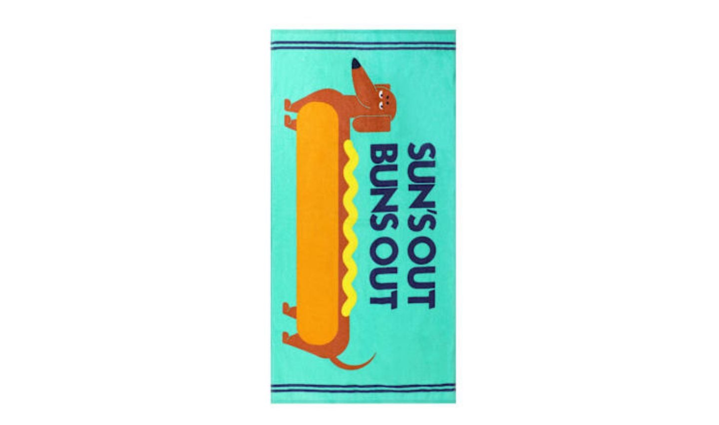 A beach towel from the new Five Below products features a cartoon dachshund resembling a hot dog in a bun, with "SUN'S OUT BUNS OUT" in bold blue letters on a light blue background.
