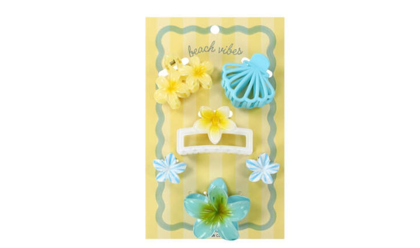 A card labeled "beach vibes" displays five pastel hair clips in floral and shell designs—one of the cute new Five Below products. The clips are blue, yellow, and white, arranged on a striped yellow background.