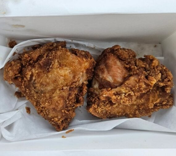 Two pieces of golden-brown fried chicken sit in a white takeout box lined with white paper.