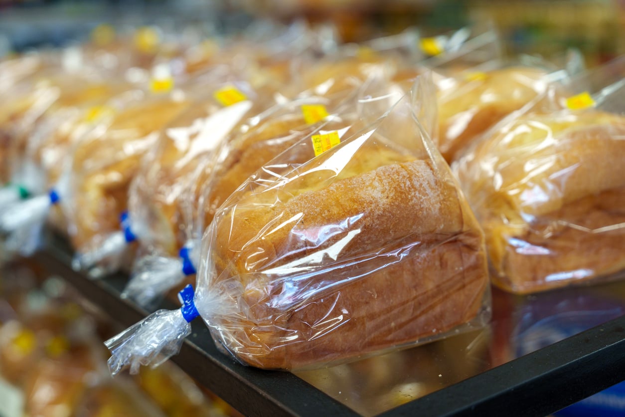 Rows of packaged loaves of bread wrapped in clear plastic bags with twist ties, displayed on a store shelf with yellow price stickers visible on each package.
