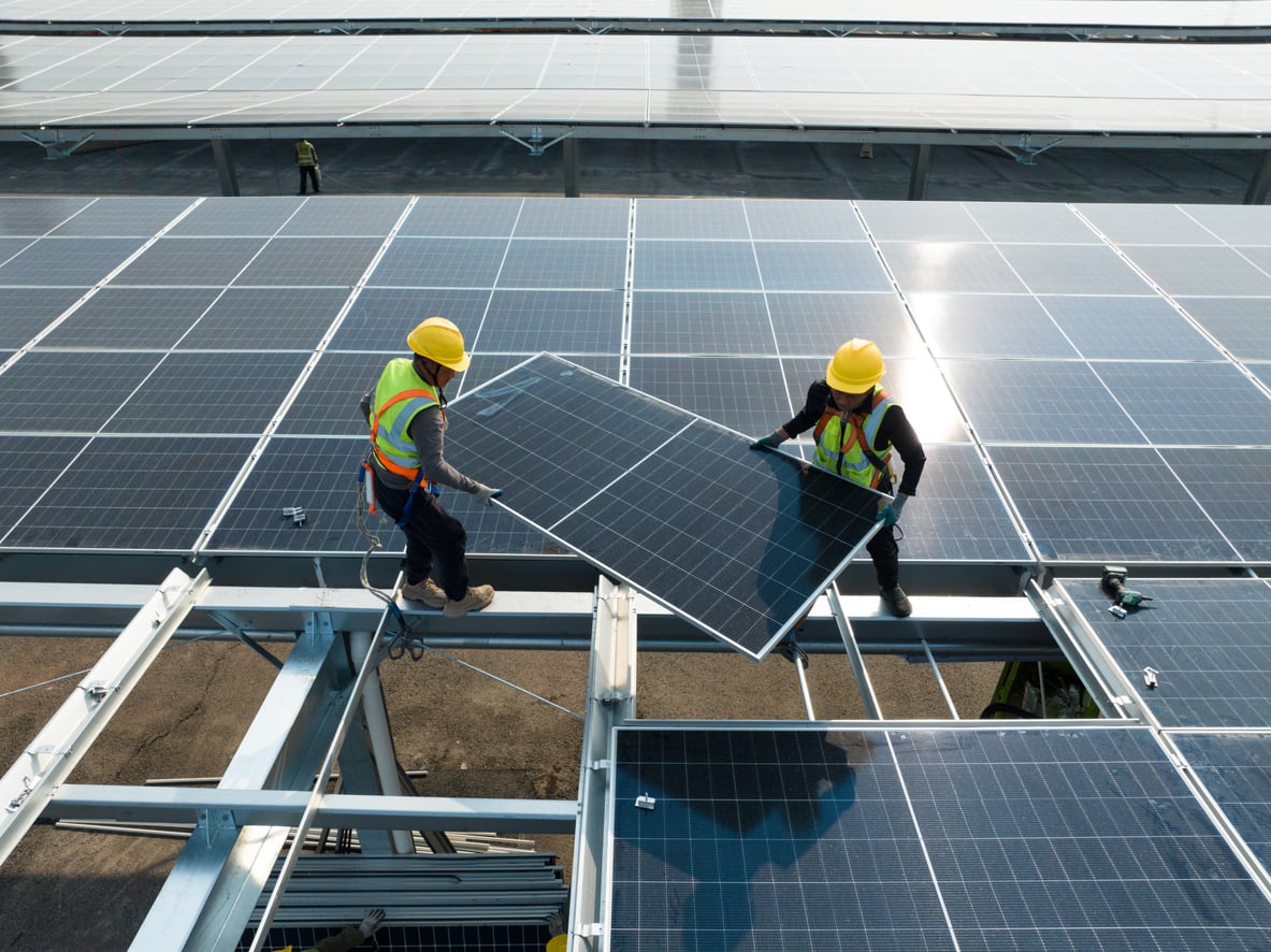 Two workers in yellow safety vests and helmets install solar panels on a large rooftop array under a bright sky—a great example of jobs you can train for in under a year, highlighting clean energy technology in action.